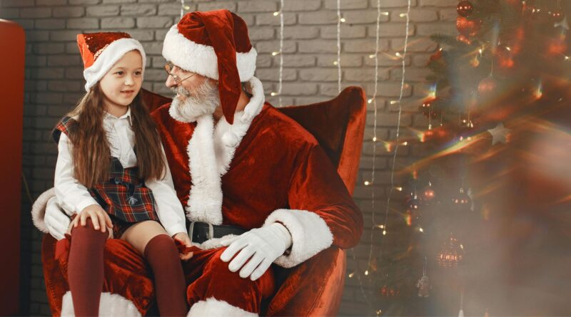 a man in santa garment sitting on a chair with a girl in a red chair